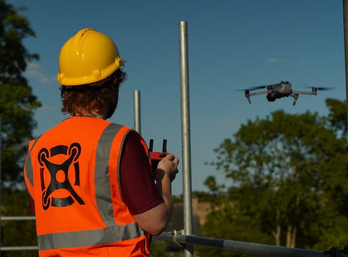 Quadrelliot operator in high-visibility clothing and a hard hat flying a drone on site